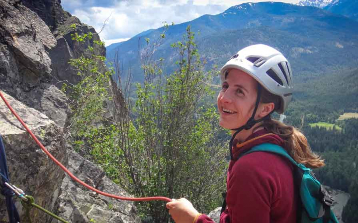 a rock climber smiles with mountains in the background
